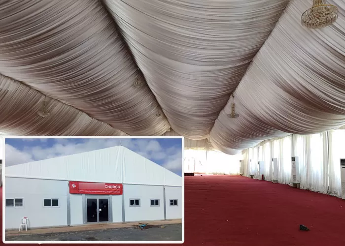 Congregation inside 25x30m revival tent during gospel service with pastor and attendees in prayer
